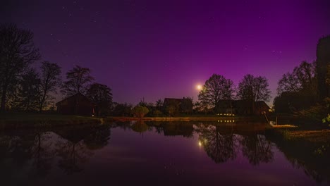 Moon-sets-over-a-countryside-cabin-by-a-pond-with-twinkling-stars-and-aurora-borealis---nighttime-time-lapse