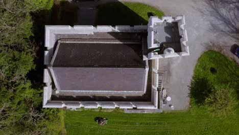 Fortified-castle-walls-and-roof-as-grounds-keeper-mows-lawn,-drone-top-down