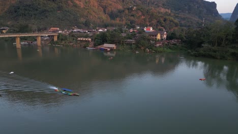 drone-shot-of-boat-on-the-river-in-the-mountain-town-of-Nong-Khiaw-in-Laos,-Southeast-Asia