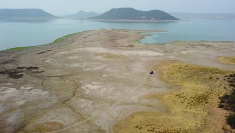 Toma-Aérea-De-Un-Dron-De-Un-Jeep-Todoterreno-Explorando-Un-Embalse-De-Un-Lago-Seco-En-La-Presa-De-Harsi-En-Gwalior,-India