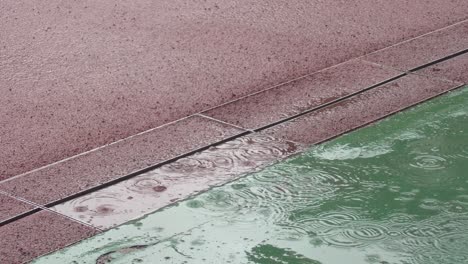 Raindrops-falling-in-puddle-falling-on-sporting-gravel-courts-in-medium-close-up