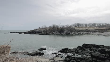 Pan-across-the-beautiful-rocky-sea-side-view-of-the-Portland-Maine-revealing-the-Head-Light-light-house-during-a-beautiful-spring-day-with-waves-rolling-into-the-rocky-shore-in-4k