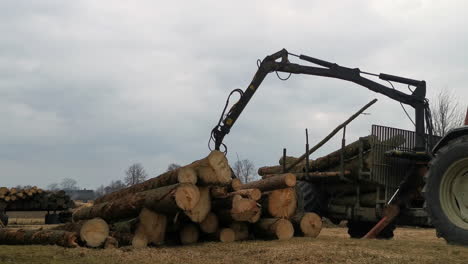 Traktor-Entlädt-An-Einem-Launischen-Tag-Baumstämme-Vom-Anhänger,-Statische-Ansicht