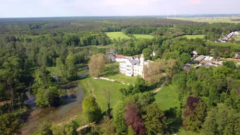 Orbit-Drone-Shot-of-the-historical-Dobra-Castle-Surrounded-By-Lush-Nature-Park-In-Dobra--Poland-on-a-sunny-day