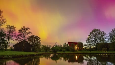 Brilliant-aurora-borealis-over-a-farm-with-the-sky-colors-reflecting-off-the-lake---time-lapse