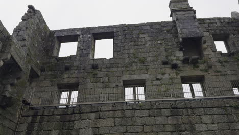 Upward-pan-across-decrepit-broken-brick-castle-walls-with-fence-on-rainy-day