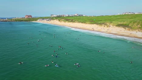 Fistral-Beach-Surfers-Sit-and-Wait-for-Ocean-Waves-in-Newquay,-Aerial-Orbital-Panning-Shot,-Cornwall,-UK