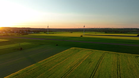 Weite-Grüne-Felder-Mit-Windrädern-Bei-Sonnenuntergang,-Entferntes-Dorf,-Goldenes-Licht,-Panoramablick
