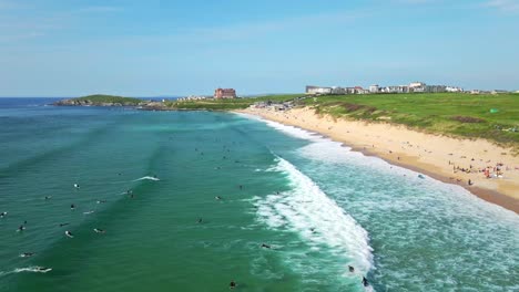 Fistral-Beach-Surfers-Riding-the-Ocean-Waves-with-Views-of-Headland-Hotel-and-Golf-Course,-Newquay,-UK