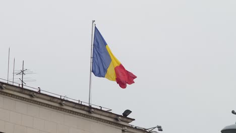 Romanian-flag-waving-on-building-against-cloudy-sky,-Bucharest