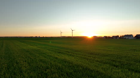 Green-fields-with-wind-turbines-at-sunset,-houses-in-distance,-serene-and-expansive