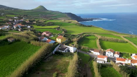 Aerial-panorama-capturing-quaint-houses-nestled-amidst-vibrant-green-fields-in-the-Azores-on-a-sunny-day,-overlooking-the-azure-expanse-of-the-Atlantic-Ocean