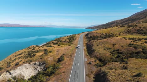 Vista-Aérea-De-Una-Furgoneta-Conduciendo-Junto-Al-Lago-Pukaki-En-Verano-En-Nueva-Zelanda