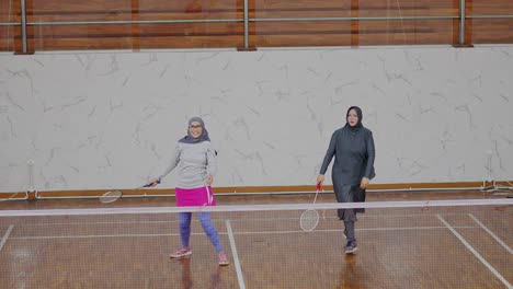 Junge-Asiatische-Muslimische-Frauen-Tragen-Sport-Hijab-Und-Spielen-Badminton-Im-Doppelspiel-Auf-Dem-Hallenplatz
