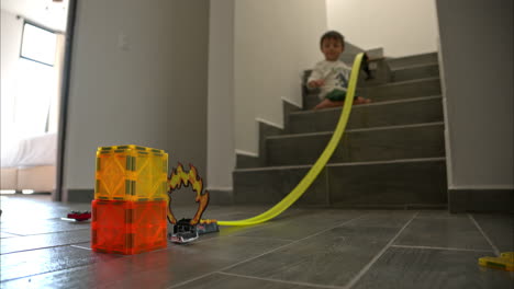 Young-mexican-latin-boy-playing-on-the-stairs-of-his-house-with-his-car-toys-using-a-long-track-and-magnet-blocks