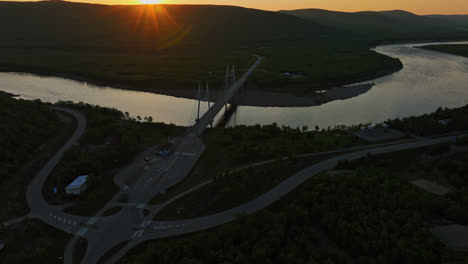 Drone-rising-toward-the-Sami-Bridge-and-the-Tenojoki-river,-midnight-sun-in-Utsjoki,-Finland