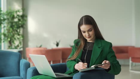 Charmante-Frau-Schreibt-In-Einem-Notizbuch,-Während-Sie-In-Der-Lobby-Eines-Business-Centers-Strahlt