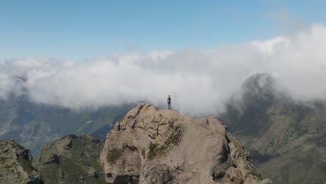 Woman-on-epic-rock-viewpoint-in-grand-mountain-range,-aerial