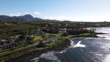 Aerial-Pan-as-Shimmering-Waves-Roll-into-Poipu,-HI-with-Mountains-on-Clear-Day