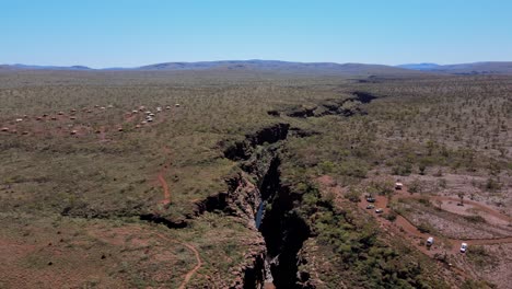 Drone-aerial-moving-back-over-Joffre-gorge-and-waterfall-in-Karijini-national-park-showing-a-resort-and-car-park