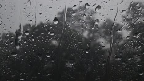 This-is-a-video-of-large-rain-drops,-landing-onto-the-window,-causing-small-streams-to-form-and-roll-down-the-window