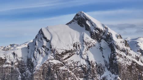 Drone-approaching-the-summit-of-Fronalpstock-mountain-in-the-Swiss-pre-Alps,-showcasing-the-blend-of-rock-and-snow