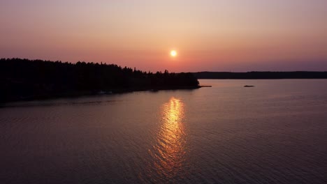 Bright-sun-setting-down-behind-silhouette-of-Stockholm-archipelago-islands,-aerial-view