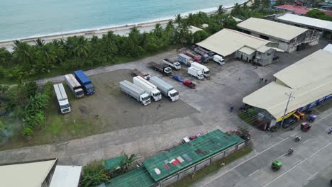 Overhead-aerial-orbit-of-cargo-trucks-parked-at-a-warehouse-parking-lot-in-Bicol-region,-Philippines