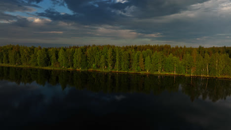Drone-shot-over-a-reflecting-lake,-toward-polar-woods,-moody-sunset-in-Lapland