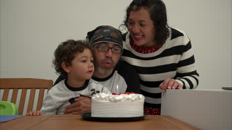 Slow-motion-of-a-hipster-alternative-mexican-family-of-three-celebrating-a-birthday-with-a-cake-and-one-candle-blowing-it