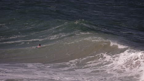 A-surfer-contends-with-large-rough-swell-off-Fingal-Head,-Northern-New-South-Wales,-Australia