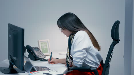 Beautiful-young-woman-with-long-dark-hair-wearing-glasses-sitting-behind-the-desk,-working-hard-at-the-work-in-office-in-slow-motion