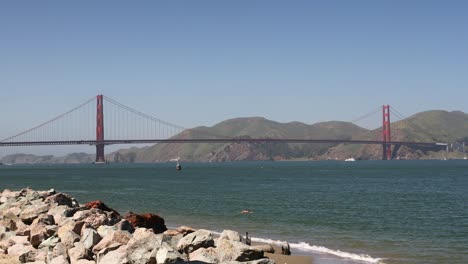 Golden-Gate-Bridge-über-Die-Bucht-Mit-Einer-Person,-Die-An-Einem-Sonnigen-Tag-In-San-Francisco,-Kalifornien,-USA-Schwimmt