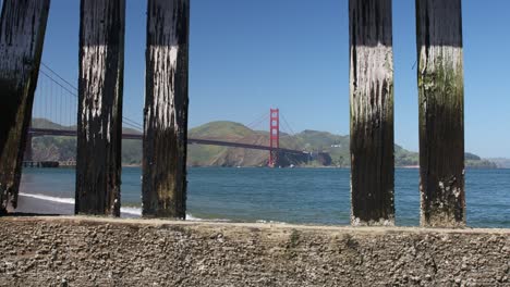 Die-Golden-Gate-Bridge,-Eingerahmt-Zwischen-Hölzernen-Pfeilern-Vor-Blauem-Himmel-Und-Ruhigem-Wasser-über-Der-Bucht,-San-Francisco,-Kalifornien,-USA