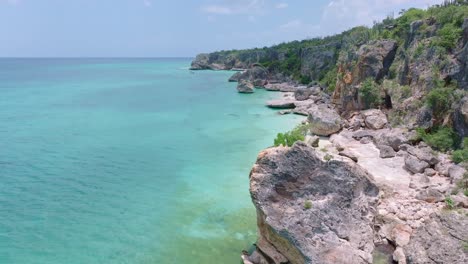 Drone-flying-at-low-altitude-over-tropical-waters-sea-along-rocky-cliff-of-Jaragua-National-Park,-Pedernales-in-Dominican-Republic