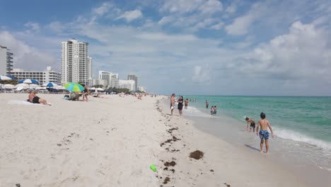 Menschen-Genießen-Einen-Sonnigen-Tag-Am-Miami-Beach-Mit-Klarem,-Blauem-Wasser-Und-Einem-Belebten-Ufer