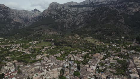 Medieval-town-Soller-surrounded-by-large-mountain-on-island-Mallorca,-aerial