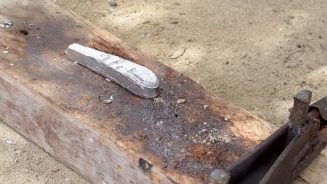 straightening-freshly-made-fishing-sinker-with-lead-using-pliers-on-wooden-board