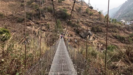 A-group-of-hikers-carefully-traverses-a-suspension-bridge,-suspended-high-above-a-mountain-valley,-on-the-stunning-Langtang-trek-in-Nepal