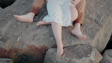 Couple-sitting-on-rocks-at-Ovar-Beach,-Portugal,-with-focus-on-their-legs-and-bare-feet