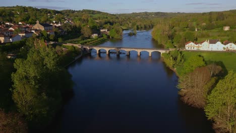 Aerial-forward-over-bridge-crossing-Vienne-River,-Saint-Victurnien,-Nouvelle-Aquitaine-in-France