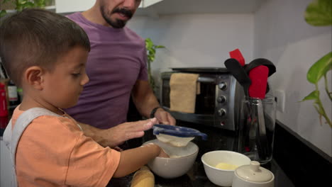 Mexican-latin-father-with-a-purple-t-shirt-cooking-in-the-kitchen-with-his-son-making-cookies-sifting-flour-slapping-a-sieve