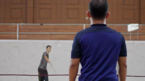 Gruppe-Von-Männern-Spielen-Badminton-Im-Doppelspiel-Auf-Dem-Sportplatz-In-Der-Halle