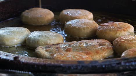 Freshly-made-Chinese-meat-pie-and-red-bean-pastry-cooking-and-sizzling-on-hot-oil-pan,-close-up-shot-of-popular-Asian-delicacy-cooking-in-process