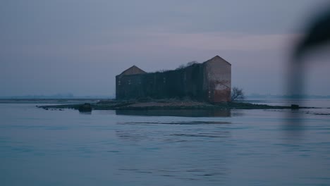 Abandoned,-rustic-building-on-a-small-island-at-dusk,-seen-from-a-boat-in-Burano,-Venice