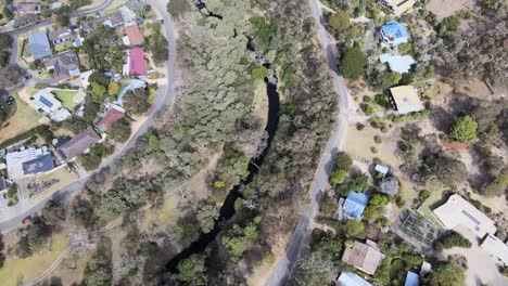 Drone-aerial-following-a-river-system-with-a-trail-in-a-suburban-town