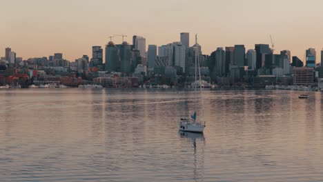 Kreisende-Aufnahme-Eines-Einsamen-Segelboots-Auf-Dem-Lake-Union-Bei-Sonnenuntergang-Mit-Skyline-Von-Seattle