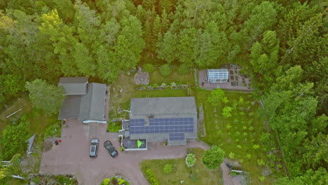 Toma-Aérea-De-Una-Casa-Aislada-Y-Alimentada-Por-Energía-Solar-En-Medio-De-Un-Bosque-Iluminado-Por-El-Sol