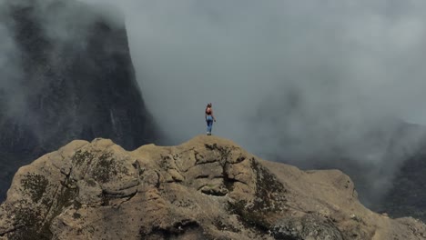 Woman-extreme-hiking-high-on-ridge-looking-at-dramatic-misty-mountains