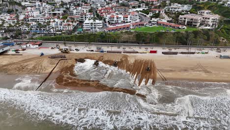 Construction-equipment-reshaping-a-beach-with-ocean-waves-in-San-Clemente's-sand-replacement-project,-aerial-view